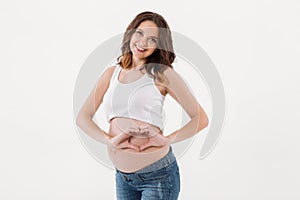 Smiling pregnant woman standing showing heart love gesture.