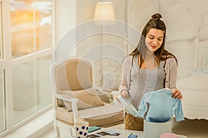 Smiling pregnant woman unpacking new children clothes