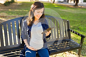 Smiling pregnant woman using a tablet in the park