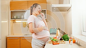 SMiling pregnant woman waiting for baby eating fresh vegetables and looking out of window on kitchen. Concept of healthy