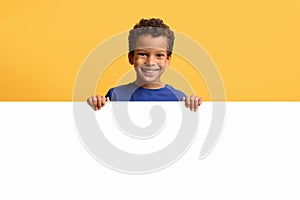 Smiling preteen african american boy hiding behind blank white placard