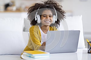 Smiling preteen black girl having video lesson, home interior