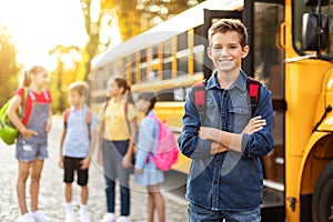 Smiling Preteen Boy Standing With Folded Arms Near Yellow School Bus