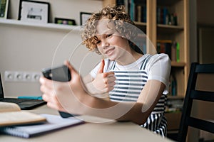 Smiling preteen girl holding and using mobile phone showing thumb up, browsing social network apps, surfing internet and