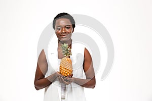 Smiling pretty african american young woman standing and holding pineapple