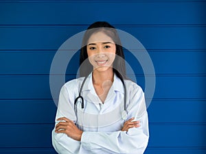 Smiling pretty Asian woman doctor portrait standing on blue wood background in medical office in hospital or clinic.