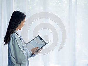 Smiling pretty Asian woman doctor portrait standing on white curtain window background in hospital room.