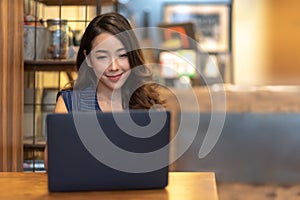 Smiling Pretty Asian woman making online reservation with laptop computer at Beautiful interior cafe. Young Charming Businesswoman
