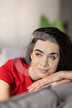 Smiling pretty young woman wearing casual clothes relaxing on a couch at home