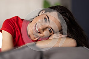 Smiling pretty young woman wearing casual clothes relaxing on a couch at home