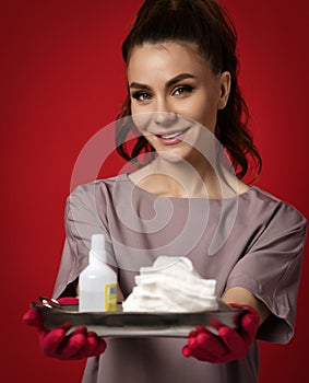 Smiling pretty brunette woman nurse doctor in red latex gloves holds medical tools, antiseptic, bandage, gauze on tray