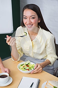 Smiling pretty businesswoman eating healthy salad