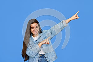 Happy Latin teen girl pointing aside at copy space standing on blue background.