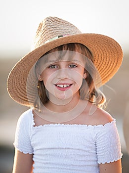 Smiling pretty girl 8-9 years old in a straw hat and a white dress Look at the camera. Summer season. Childhood