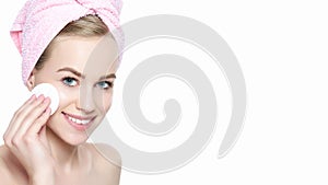 Smiling pretty girl with perfect complexion cleansing her face using soft cosmetic cotton pad