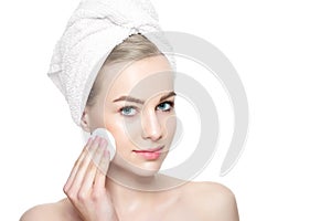 Smiling pretty girl with perfect complexion cleansing her face using soft cosmetic cotton pad. Isolated on white background