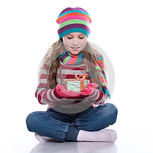 Smiling pretty little girl wearing coloful knitted scarf, hat and gloves, holding christmas gift isolated on white background. Win photo