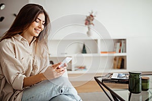 Smiling pretty millennial mixed race woman looking at phone, reading message, chatting, surfing in internet