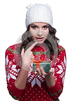 Smiling pretty young woman wearing colorful knitted sweater with christmas ornament and hat, holding christmas gift.