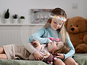 Smiling pretty small girls loving sisters in warm knitted home clothes and accessories on heads relaxing together in bedroom
