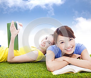 Smiling pretty students lying on the grassland with books
