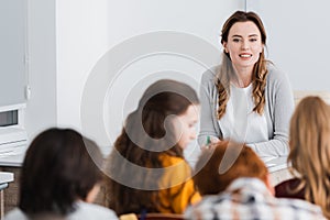 smiling, pretty teacher near schoolkids on