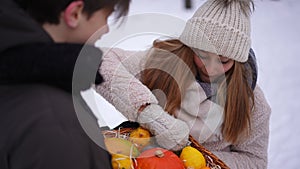 Smiling pretty teenage girl talking with boy choosing fruit from wicker basket. Portrait of happy relaxed Caucasian