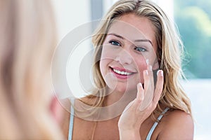 Smiling pretty woman applying cream on her face