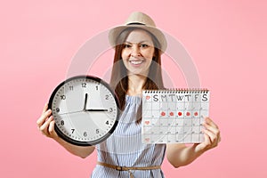 Smiling pretty woman in blue dress, hat holding round clock, periods calendar for checking menstruation days isolated on