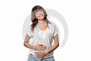 A smiling pretty woman in casual clothes holds her stomach with hands. White background. Concept of good digestion and helthy