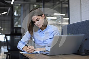 Smiling pretty woman sits at table. Happy entrepreneur writes notes to clients