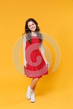 Smiling pretty young brunette woman girl in red summer dress posing isolated on yellow wall background studio portrait