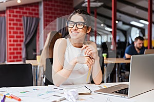 Smiling pretty young business woman in glasses sitting on workplace