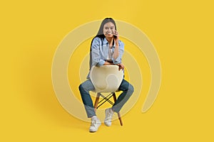 Smiling pretty young chinese woman student in casual sitting on chair and looking at camera