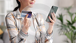 Smiling pretty young Indian brunette girl holding mobile phone and credit card sitting at the table. Happy woman makes