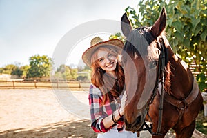 Smiling pretty young woman cowgirl in hat with her horse