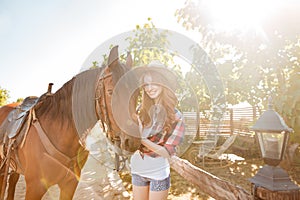 Smiling pretty young woman cowgirl in hat with her horse