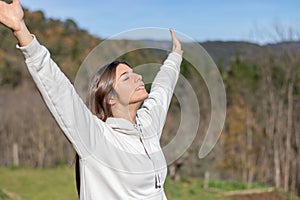 Smiling pretty young woman with sweatshirt breathing clean air in nature and sunbathing