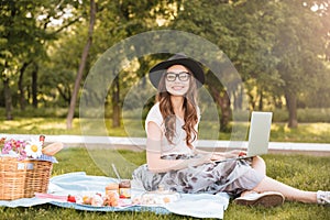 Smiling pretty young woman using laptop on picnic in park