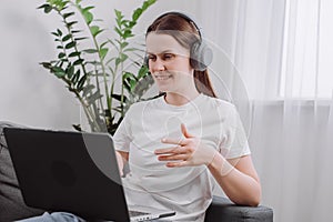 Smiling pretty young woman wear wireless headset using laptop for e learning course online teaching in internet, happy girl 25s