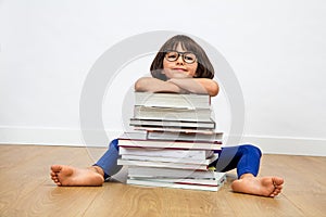 Smiling primary child with eyeglasses leaning on pile of books