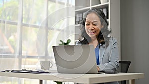 A smiling Asian senior businesswoman working on her business work on her laptop