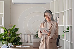 Smiling professional business woman entrepreneur holding digital tablet pad standing in office at work