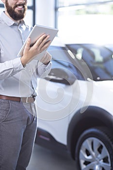 Smiling professional car dealer with tablet in exclusive showroom