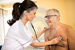 Smiling professional feamle doctor examining senior man with ste photo