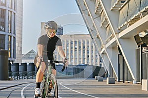 Smiling professional female cyclist in black cycling garment and protective gear looking satisfied with her exersicing