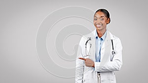 Smiling professional millennial black doctor point finger to copy space, recommends exam, sale