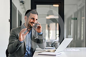 Smiling professional talking on smart phone while sitting at desk in office