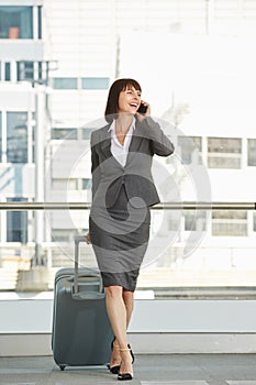 Smiling professional woman with suitcase and smart phone