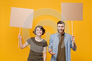 Smiling protesting young two people guy girl hold protest signs broadsheet blank placard on stick isolated on yellow